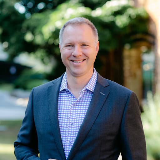 Jeremy Strickler smiling outdoors in a gray jacket and checked shirt